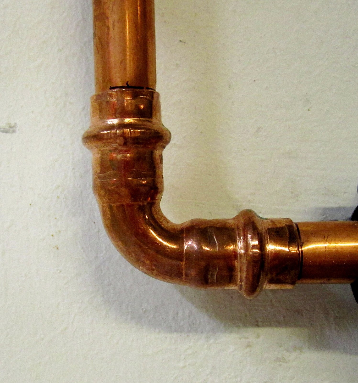 A copper supply pipe turning a right angle through a press-fit elbow on a white wall