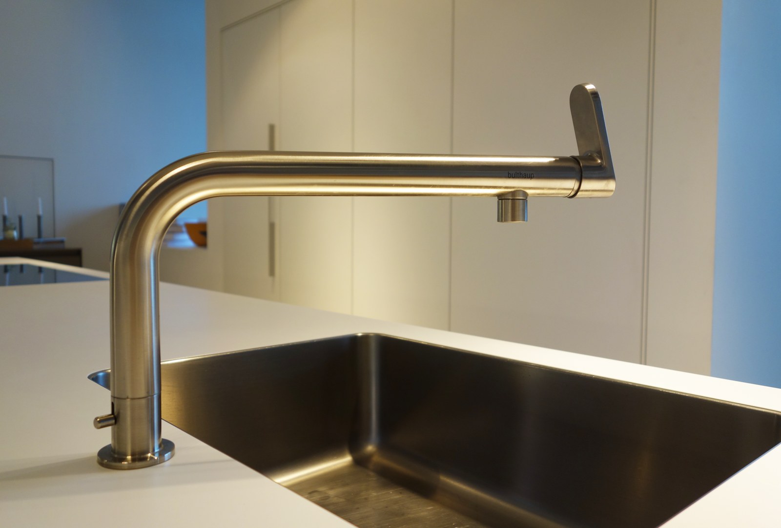 A brushed steel kitchen tap arched over an undermount sink in a white counter
