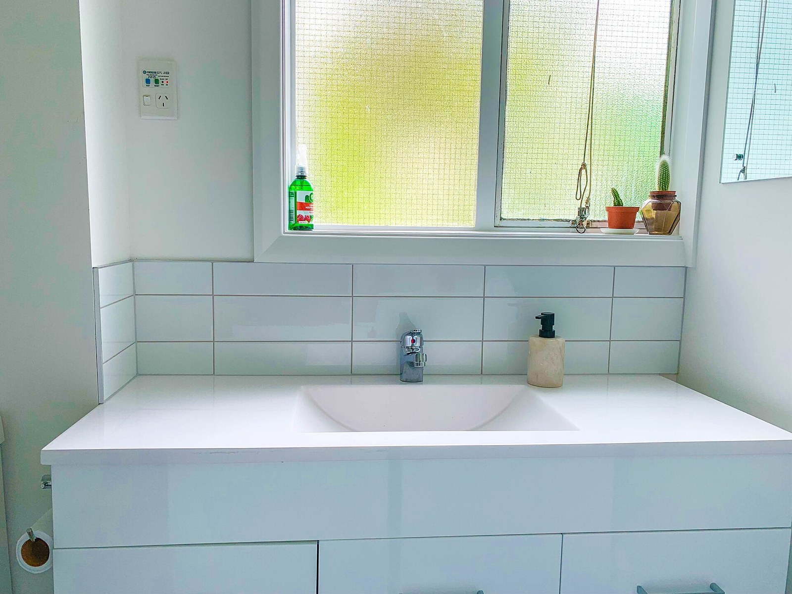 A white vanity unit with an undermount basin and chrome tap below a frosted window