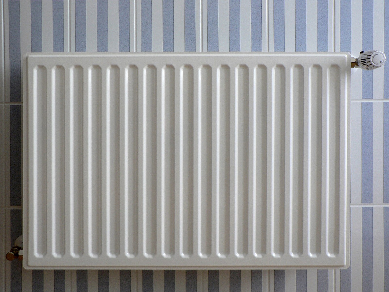A white panel radiator on a wall, with a thermostatic valve at the right-hand end