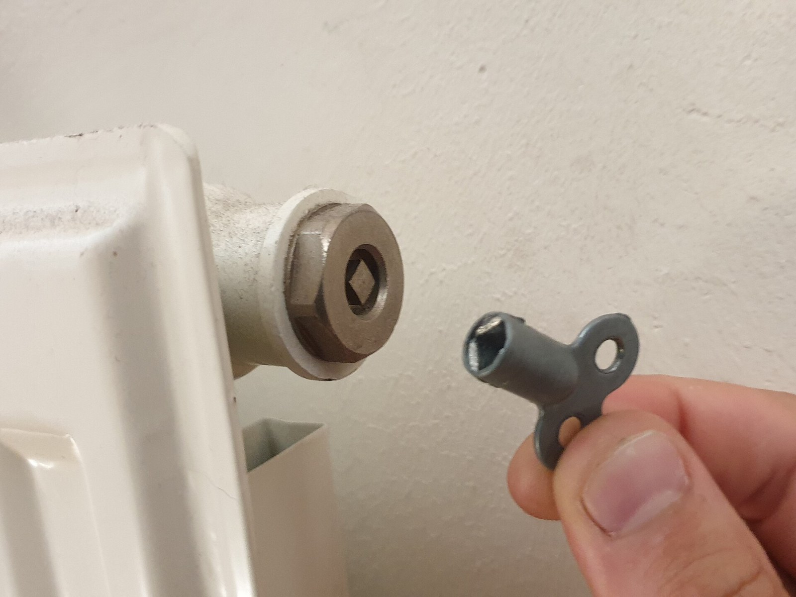 A hand holding a bleed key to the bleed valve at the top corner of a radiator