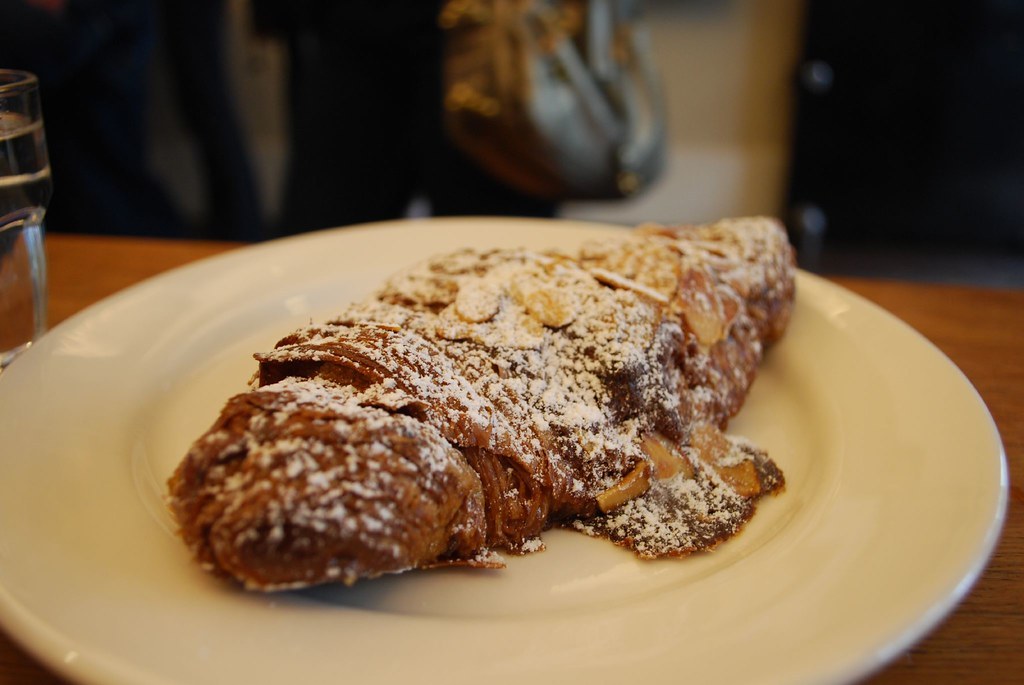 An almond croissant on a white plate, dusted with icing sugar and flaked almonds