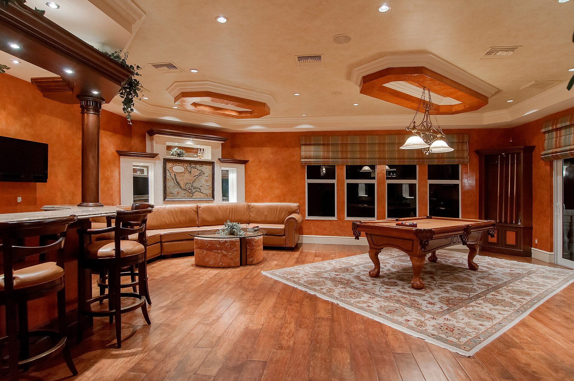 A large games room with recessed ceiling lights, a pendant over a pool table and a bar.