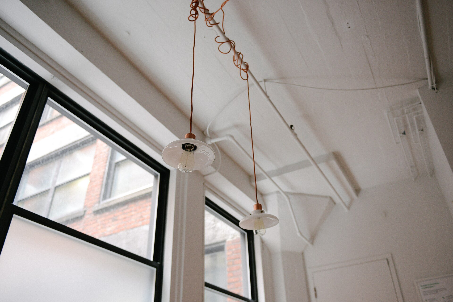 Two white pendant lights on copper cords hanging beside tall steel-framed windows.