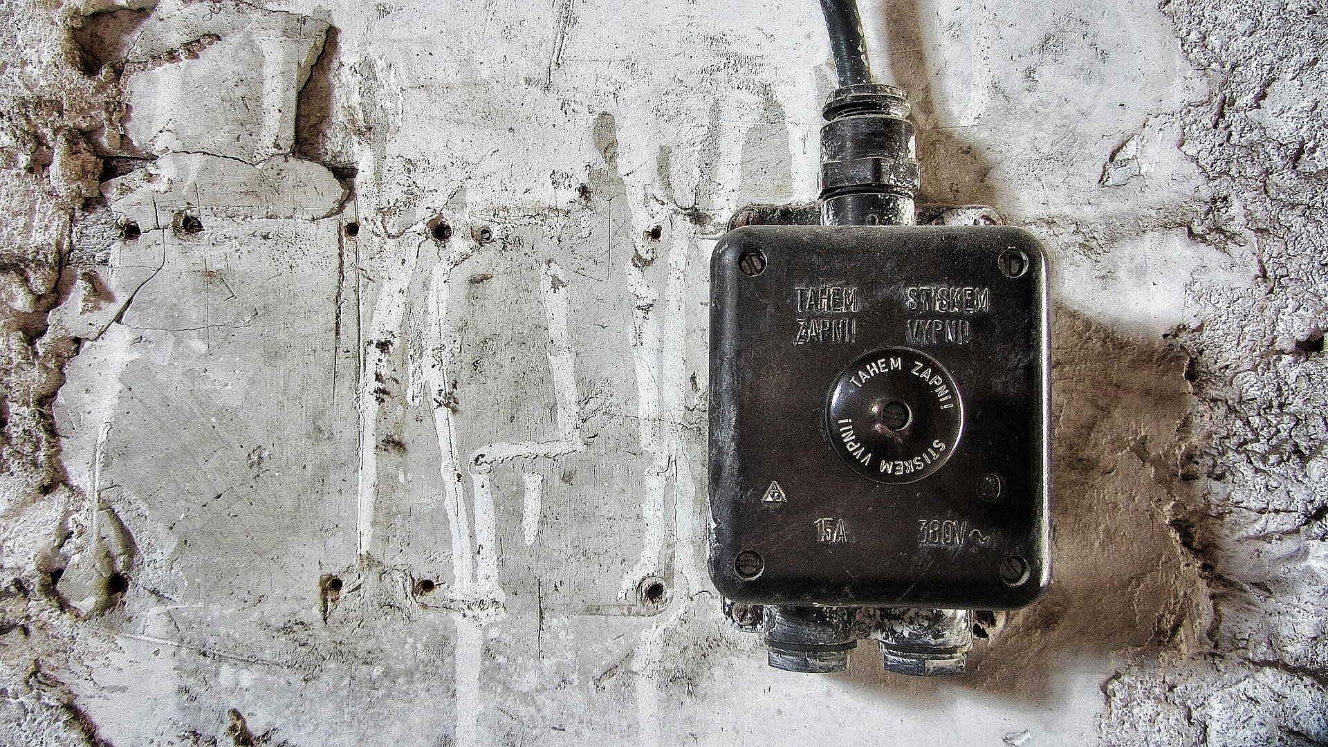 A black surface-mounted switch box with a cable entry on a rough plaster wall.