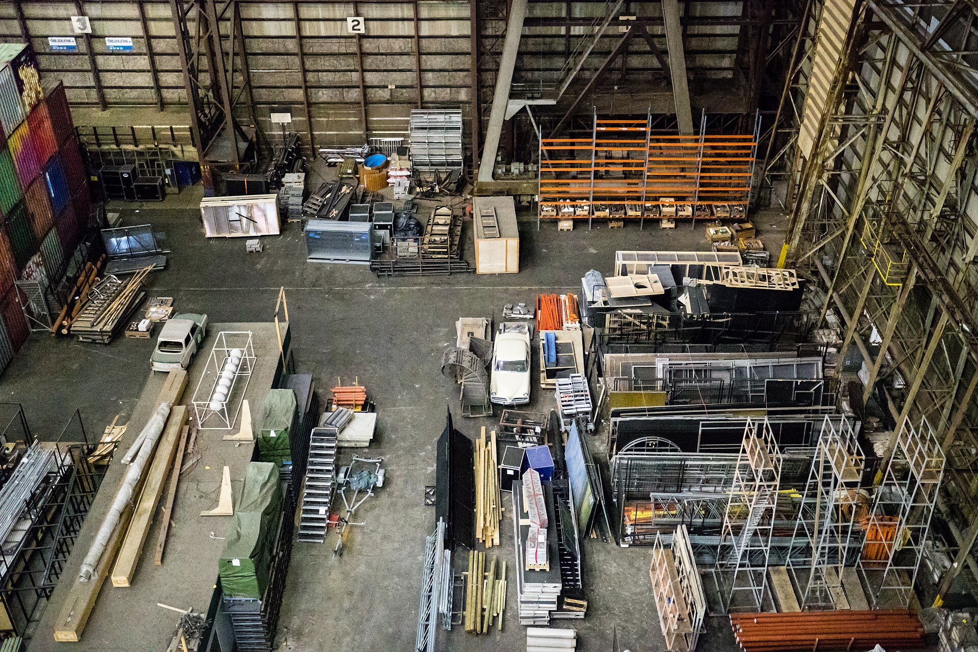 A high-bay warehouse floor seen from above, with racks, crates and stacked materials.