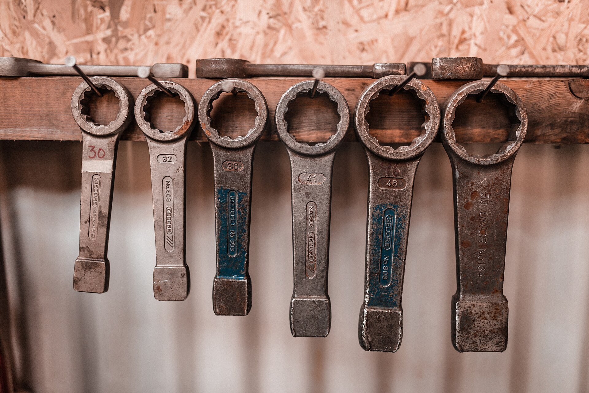 A row of heavy ring spanners hanging on a wooden rack.