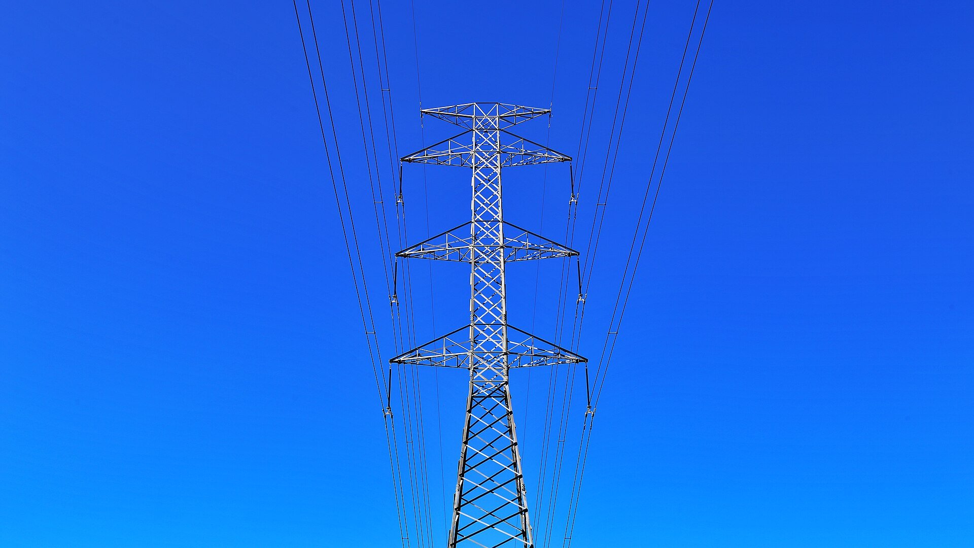 A steel transmission tower carrying power lines against a clear blue sky.